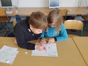 Zwei Kinder sitzen an einem Tisch und lösen gemeinsam Aufgaben auf einem Blatt Papier.