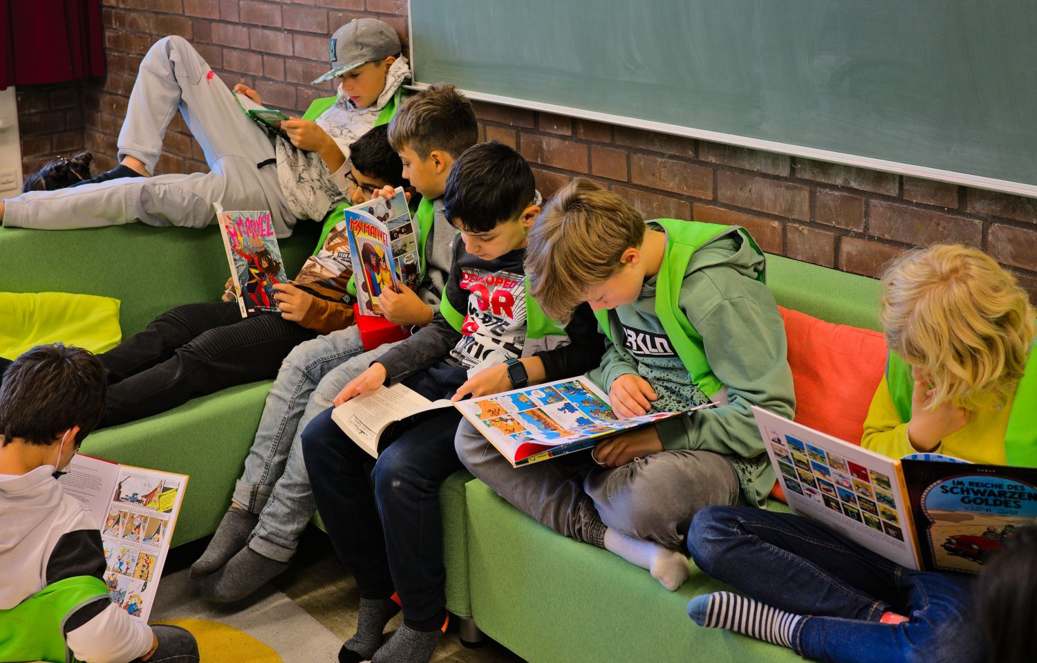 Kinder sitzen auf einem grünen Sofa und lesen in Büchern.